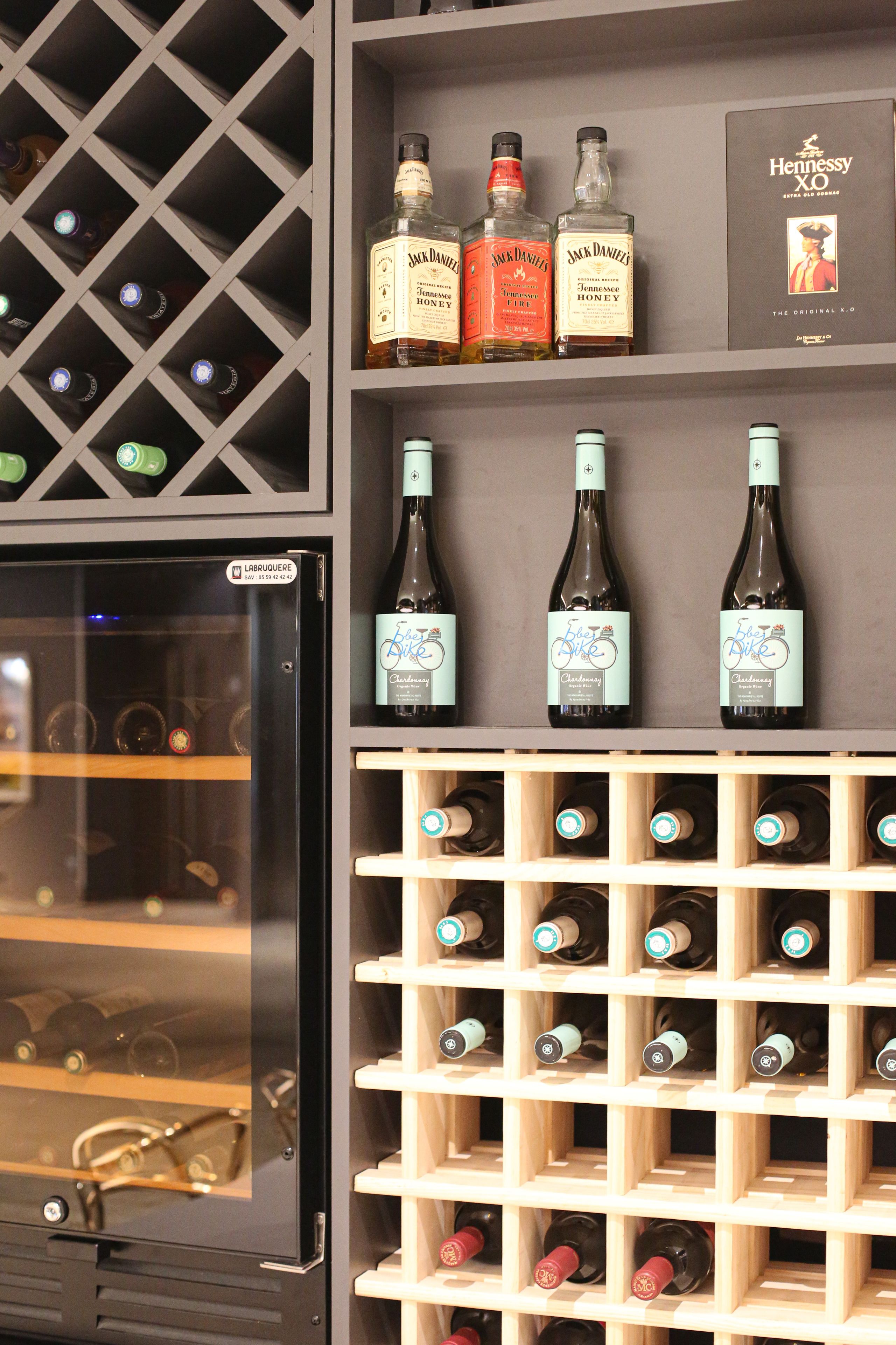 Una dispensa per vino con diverse bottiglie, un frigorifero e un libro intitolato "Hennessy XO".