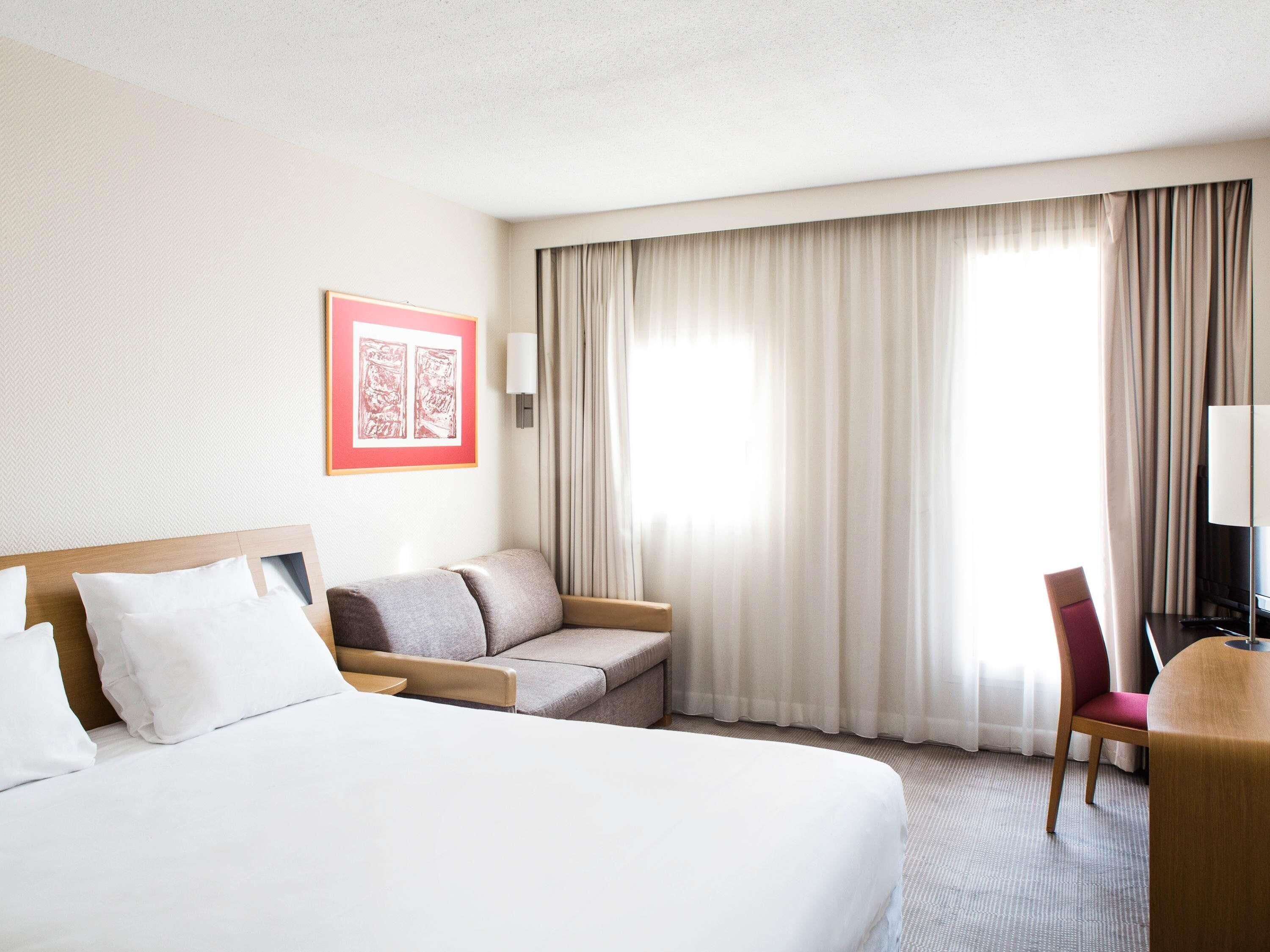 A hotel room with a large bed, a sofa, a chair, and a desk with a lamp.