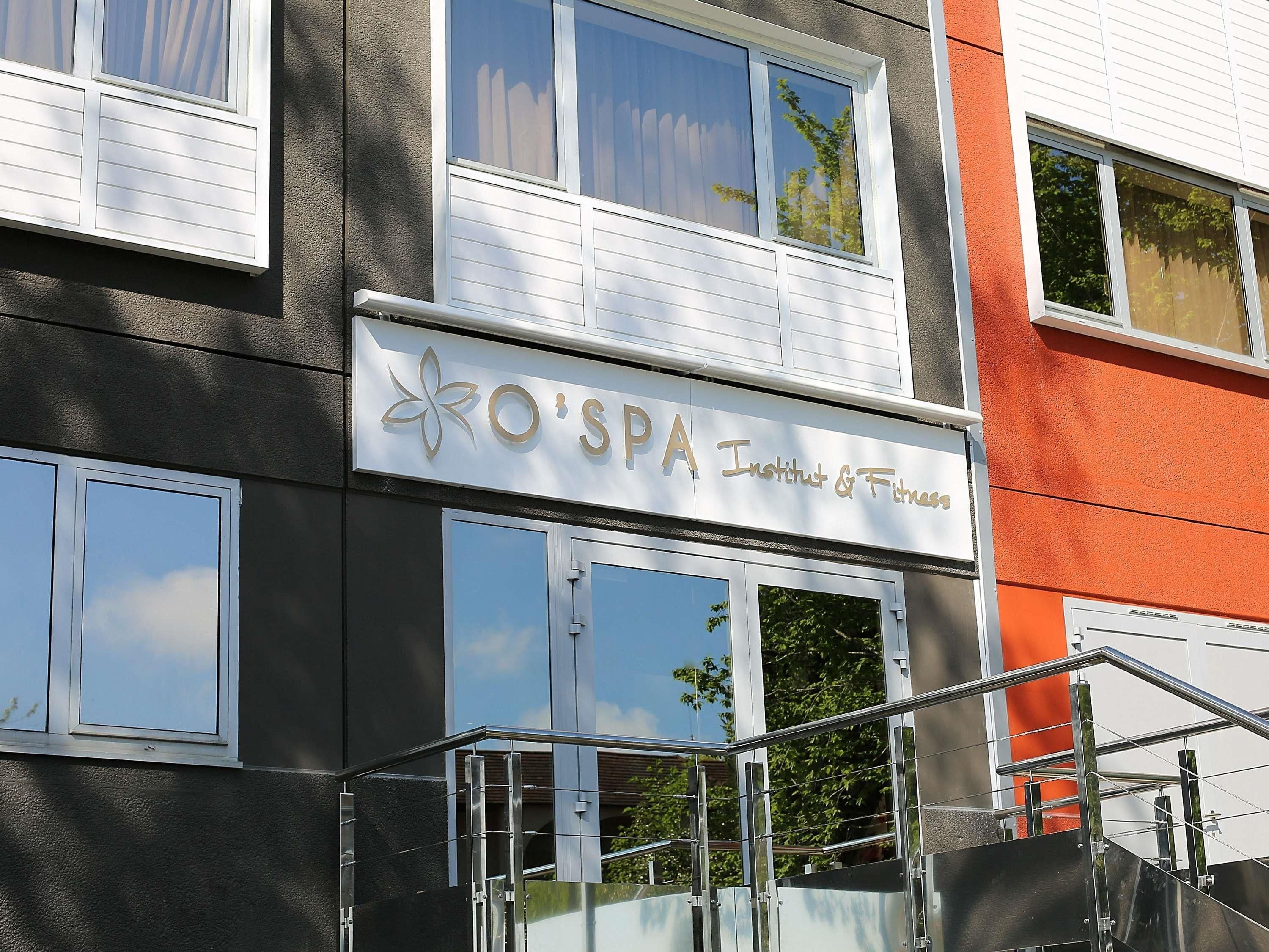 Un edificio con un letrero que dice 'O'SPA Institut & Fitness' y ventanas grandes.