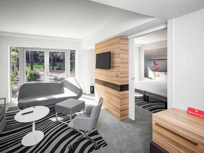 A modern hotel room with a large window, a flat-screen TV, a bed, a desk, and a chair. - Novotel Resort & Spa Biarritz Anglet (Anglet)