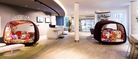 A modern spa reception area with a curved ceiling, a reception desk, and two floral-patterned seating areas.