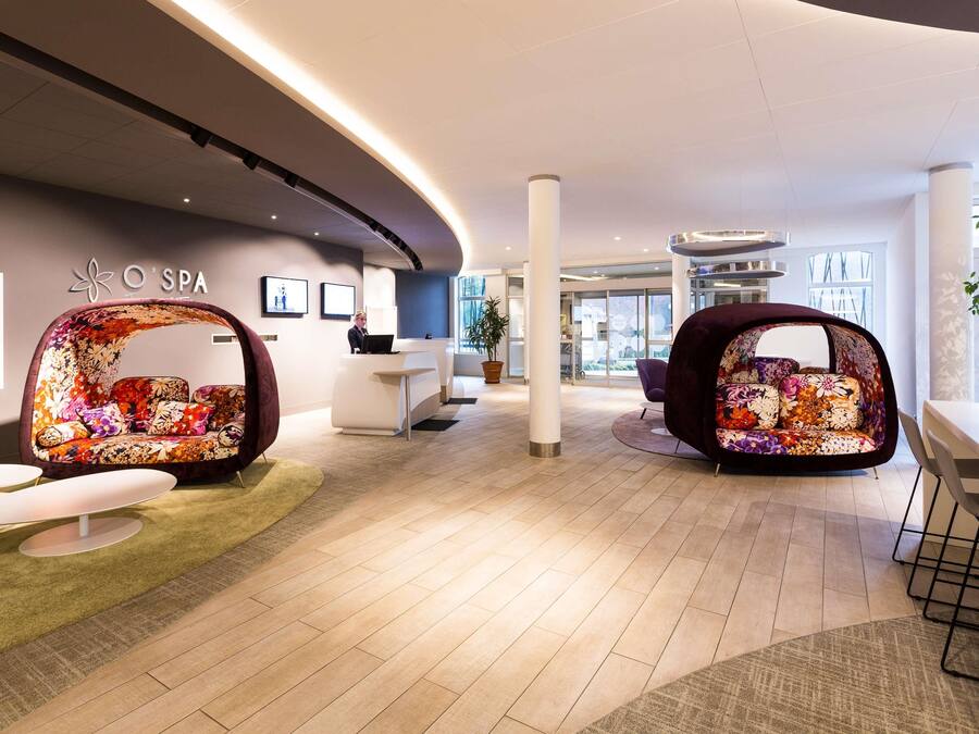 A modern spa reception area with a curved ceiling, a reception desk, and two floral-patterned seating areas.