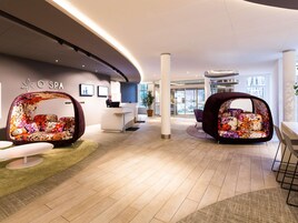 Uma área de receção de spa moderna com teto curvo, balcão de receção e duas áreas de estar com padrão floral.