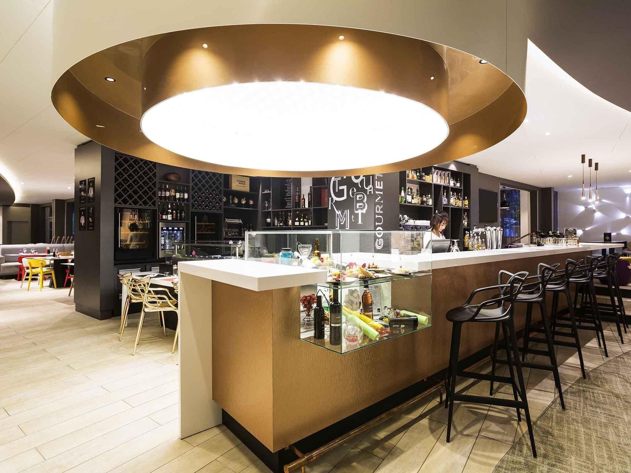 Un espace bar moderne avec un comptoir central, des tabourets de bar et un barman.