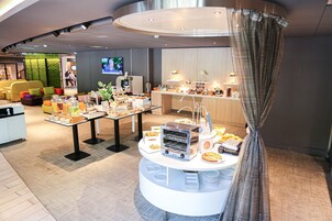 Un moderno vestíbulo de hotel con zona de buffet, asientos y una pantalla de televisión.