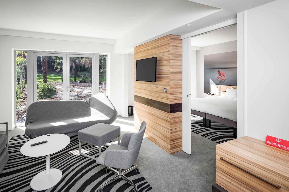 Une chambre d’hôtel moderne dotée d’une grande fenêtre, d’un téléviseur à écran plat, d’un lit, d’un bureau et d’une chaise.