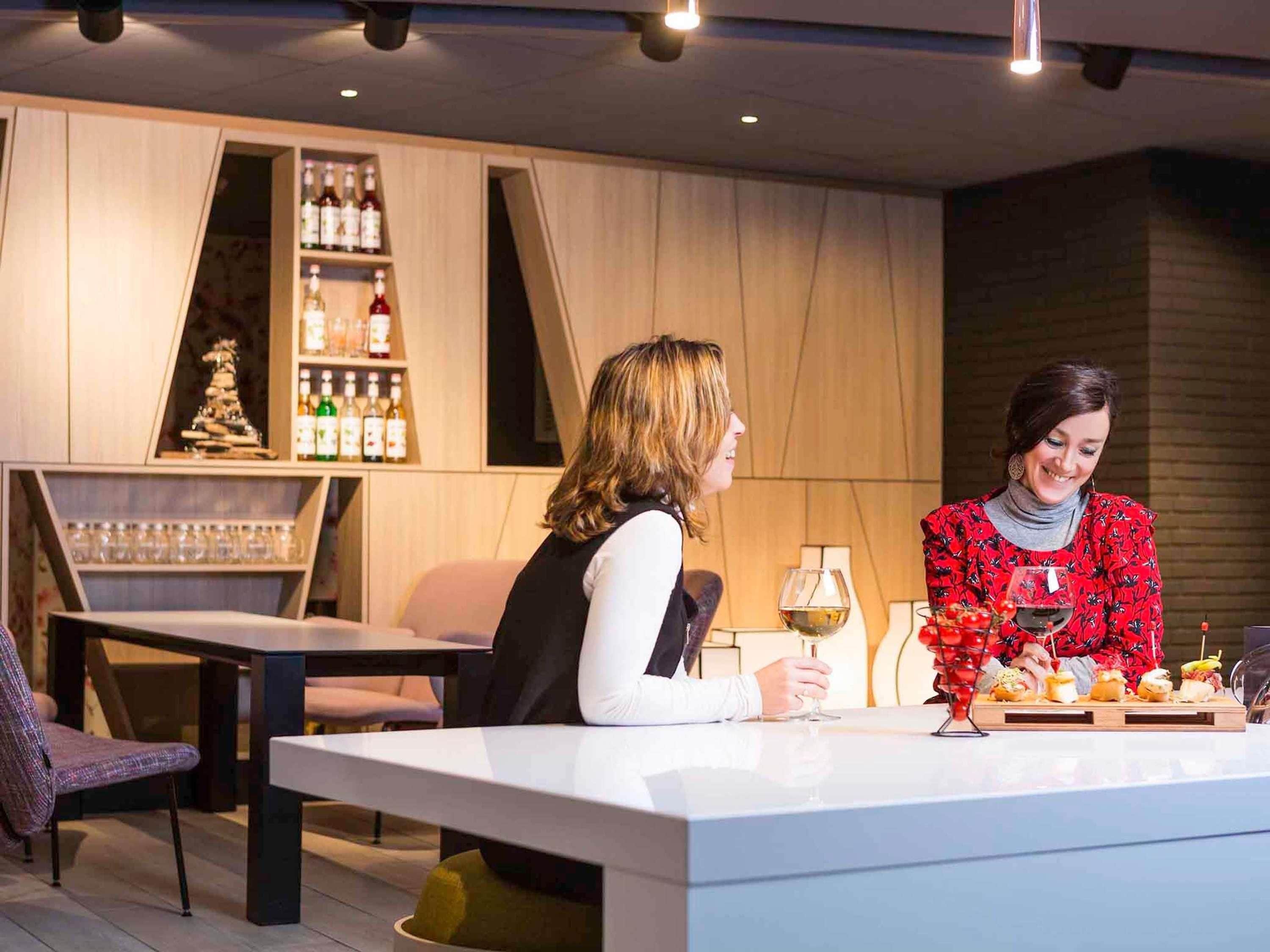 Un área de bar moderna con estantes llenos de botellas y vasos, una barra con una bandeja de comida y un espacio de asientos con una silla y una mesa.