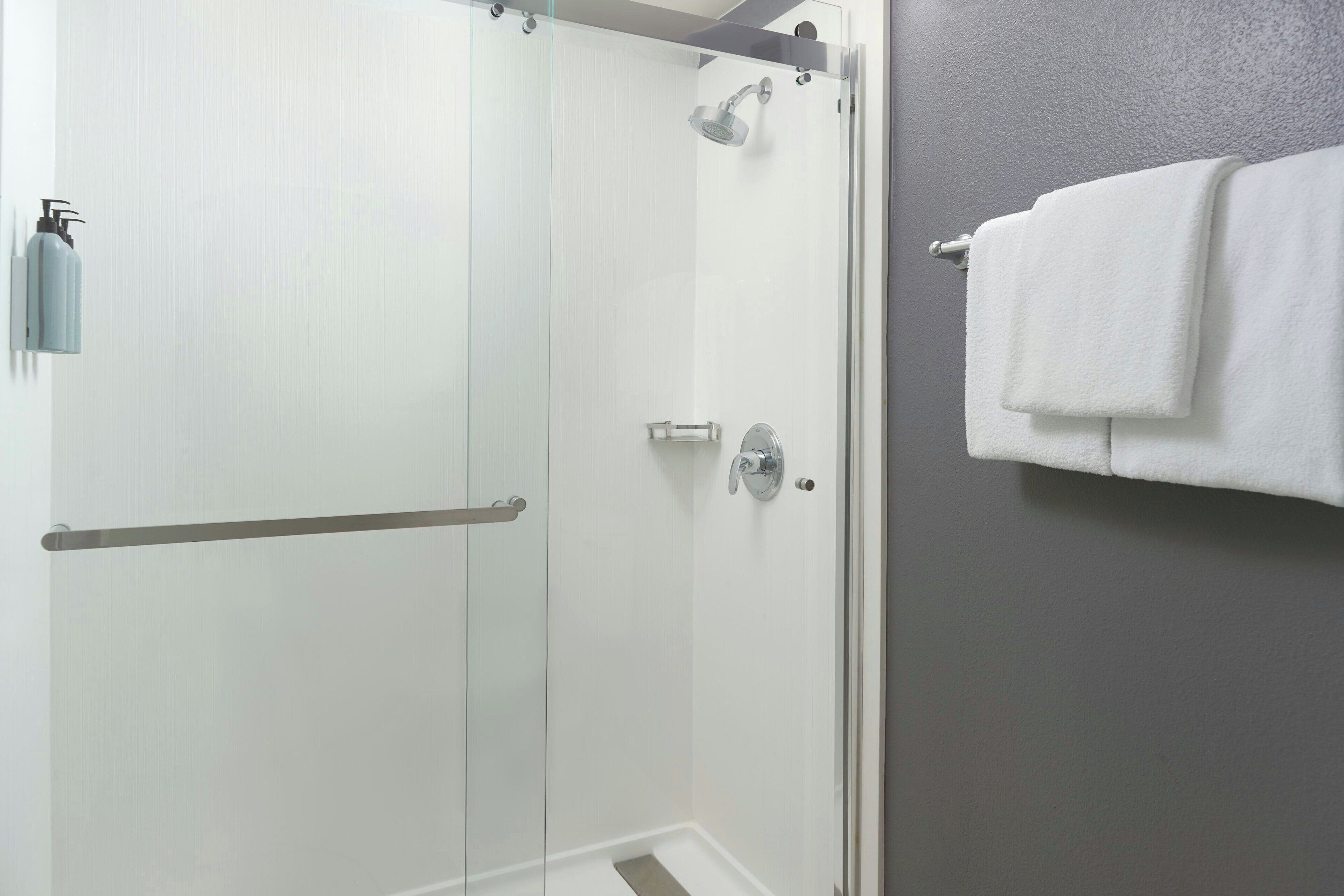 A modern bathroom with a glass shower enclosure, a towel rack, and a soap dispenser.
