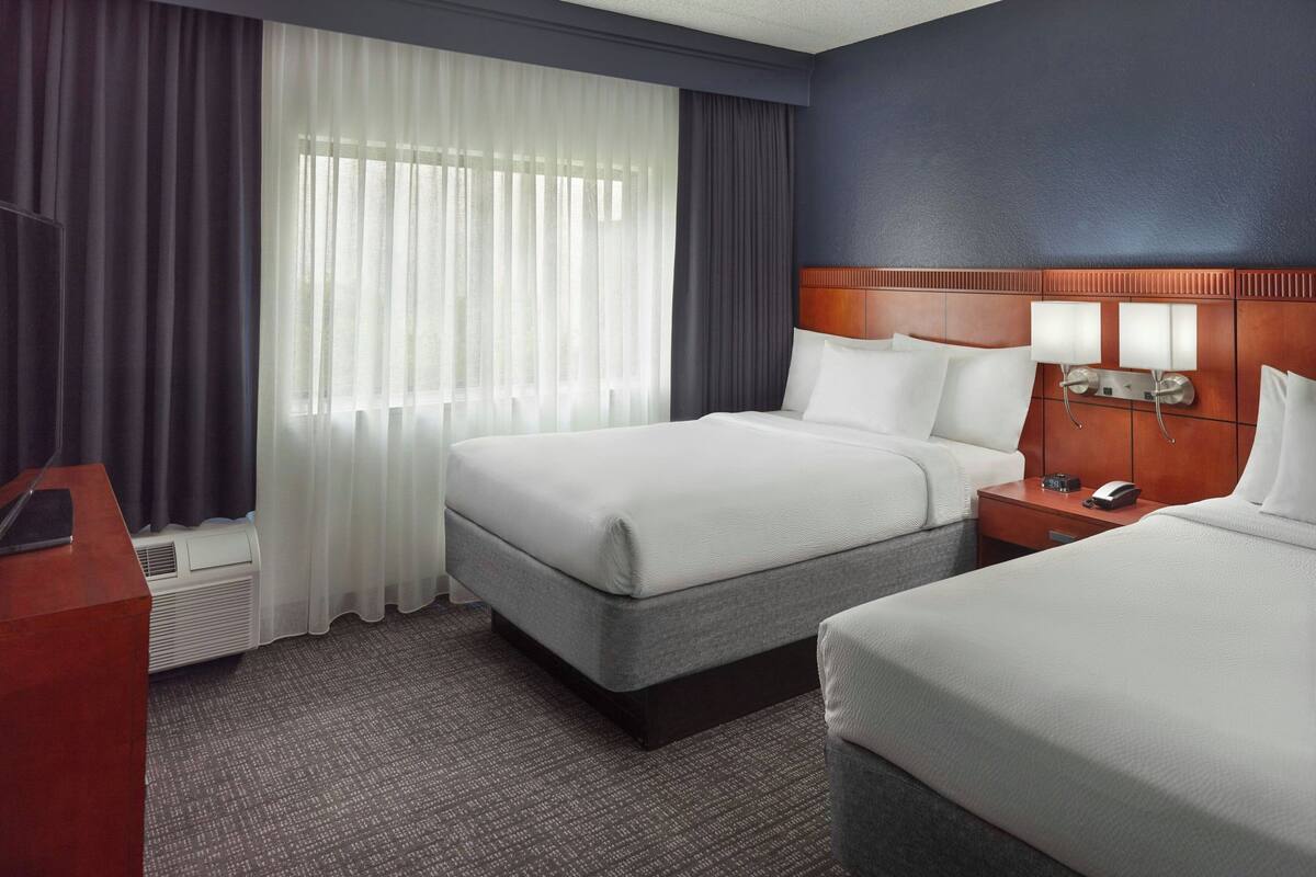 Een hotelkamer met twee bedden, een bureau en een raam met gordijnen.