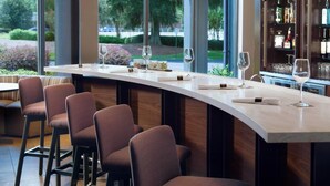 A bar area with a curved counter, bar stools, and a wine glass. - Courtyard by Marriott Tallahassee Downtown/Capitol (Tallahassee)