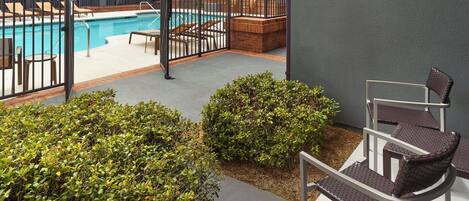 A pool area with a fenced section, outdoor seating, and greenery.