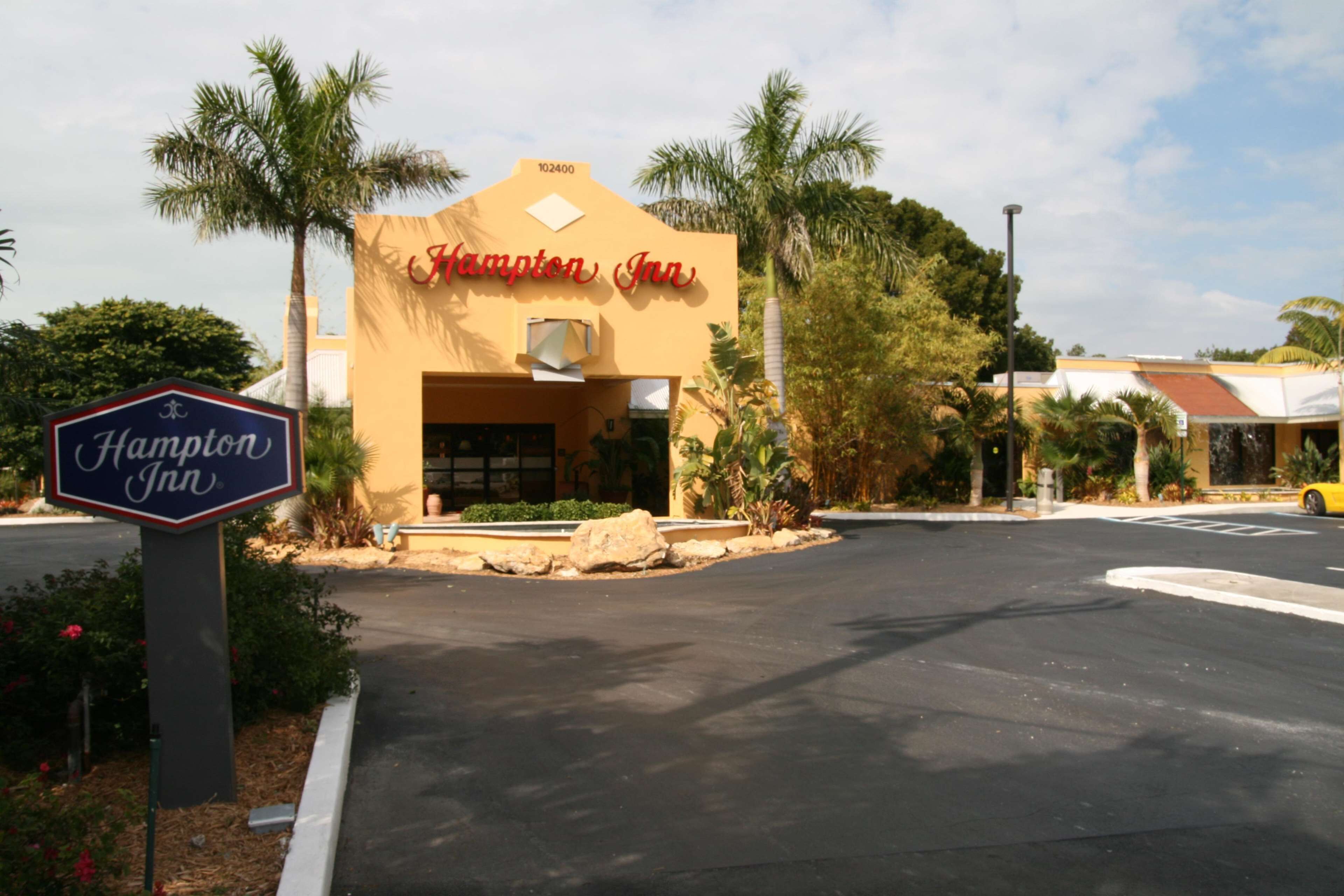 A Hampton Inn building with a sign, palm trees, and a parking lot.