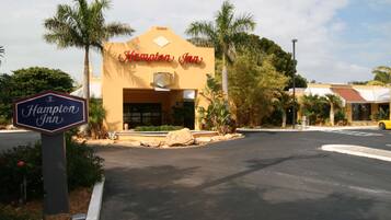 A Hampton Inn building with a sign, palm trees, and a parking lot.