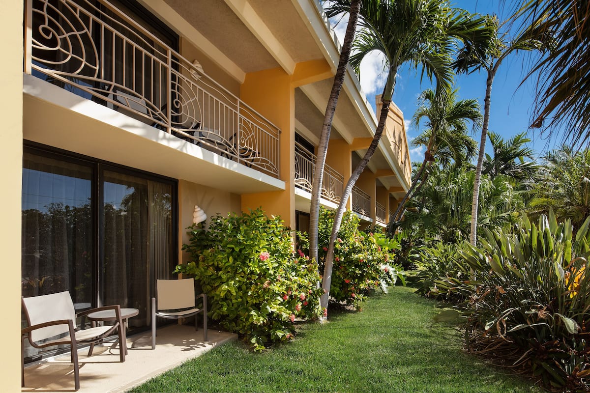 A hotel with a balcony, outdoor seating, and lush greenery.