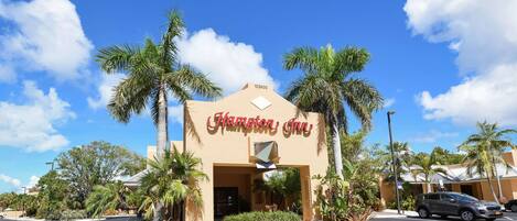 The exterior of Hampton Inn with a clear sky, palm trees, and a parking lot.