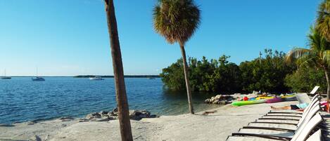 A beach with lounge chairs, kayaks, and boats on the water.