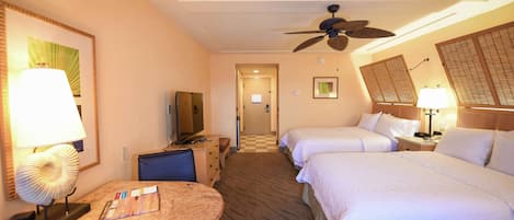 A hotel room with two beds, a desk with a lamp, a television, and a ceiling fan.