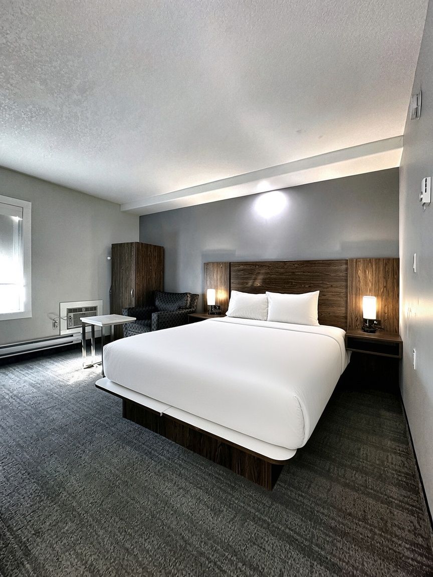 Camera d'albergo con un letto grande, una scrivania, una sedia e un comodino con lampade.
