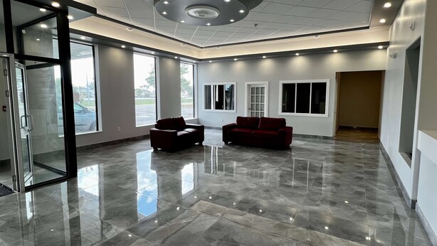 Un vestíbulo amplio con piso de mármol pulido, dos sofás rojos y una entrada con puerta de vidrio.