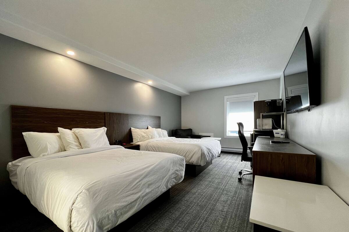 Habitación de hotel con dos camas, un escritorio, una silla, un televisor y una ventana.