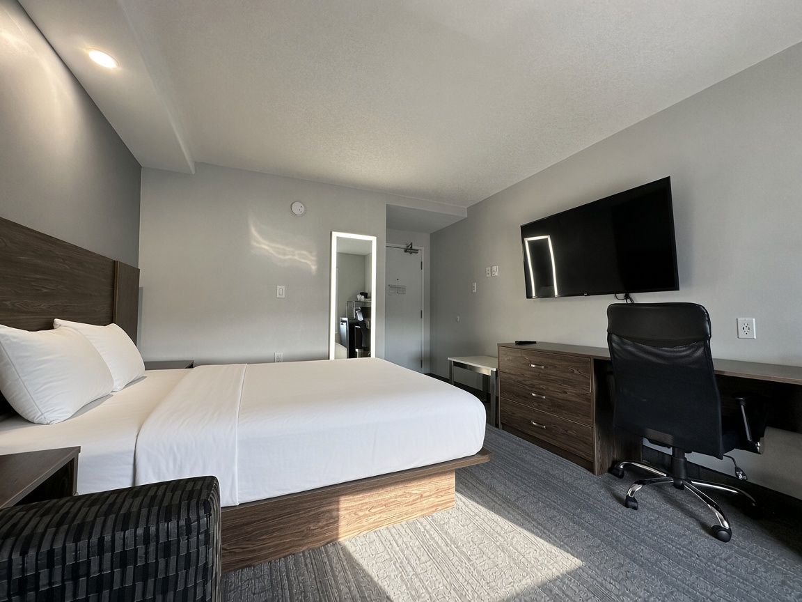 A modern hotel room with a large bed, a desk, a chair, a flat-screen TV, and a walk-in closet.