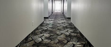 Un long couloir étroit, doté d’un tapis à motifs et de murs blancs.