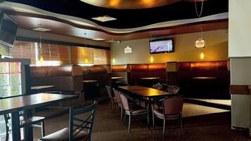 Interior de un restaurante con cabinas, mesas y una pantalla de televisión mostrando un partido de hockey.