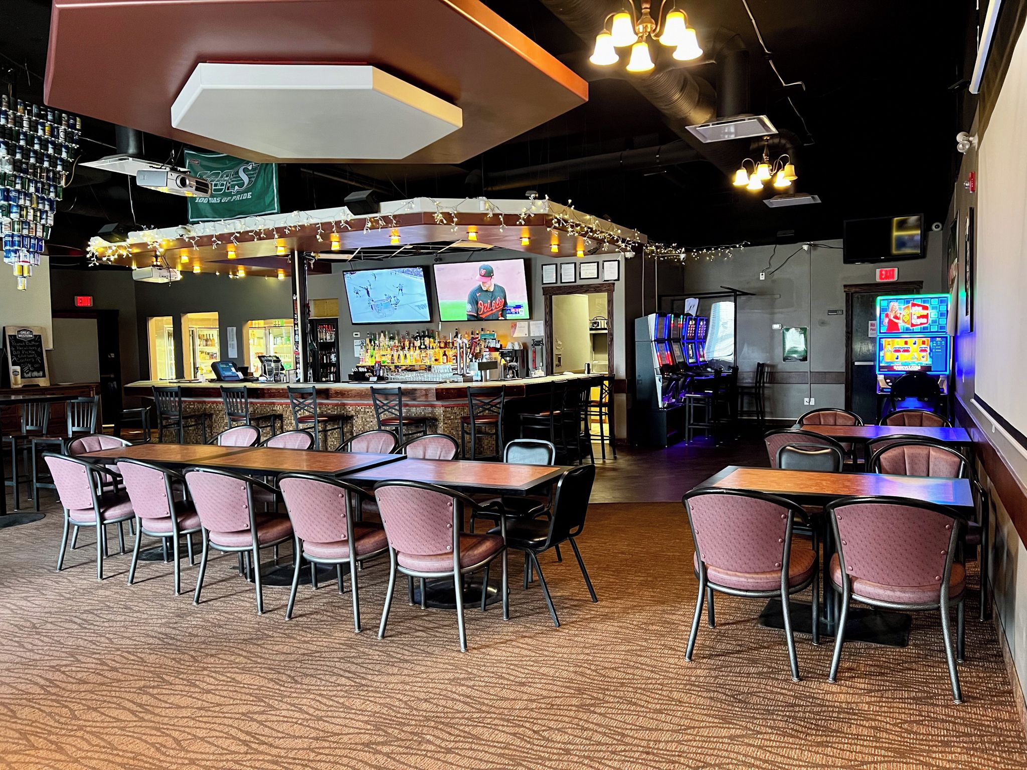 Zona de bar con diversas opciones de asientos, incluyendo mesas y sillas, además de una barra con una variedad de botellas y una pantalla de televisión.