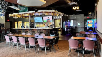 Zona bar con varie opzioni di seduta, tra cui tavoli e sedie, e un bancone bar con una selezione di bottiglie e uno schermo televisivo.