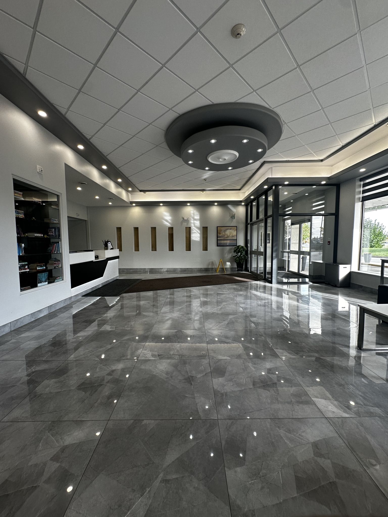 Un hall d’entrée spacieux avec un plafond haut, des luminaires encastrés, un comptoir de réception et une grande porte vitrée donnant sur l’extérieur.