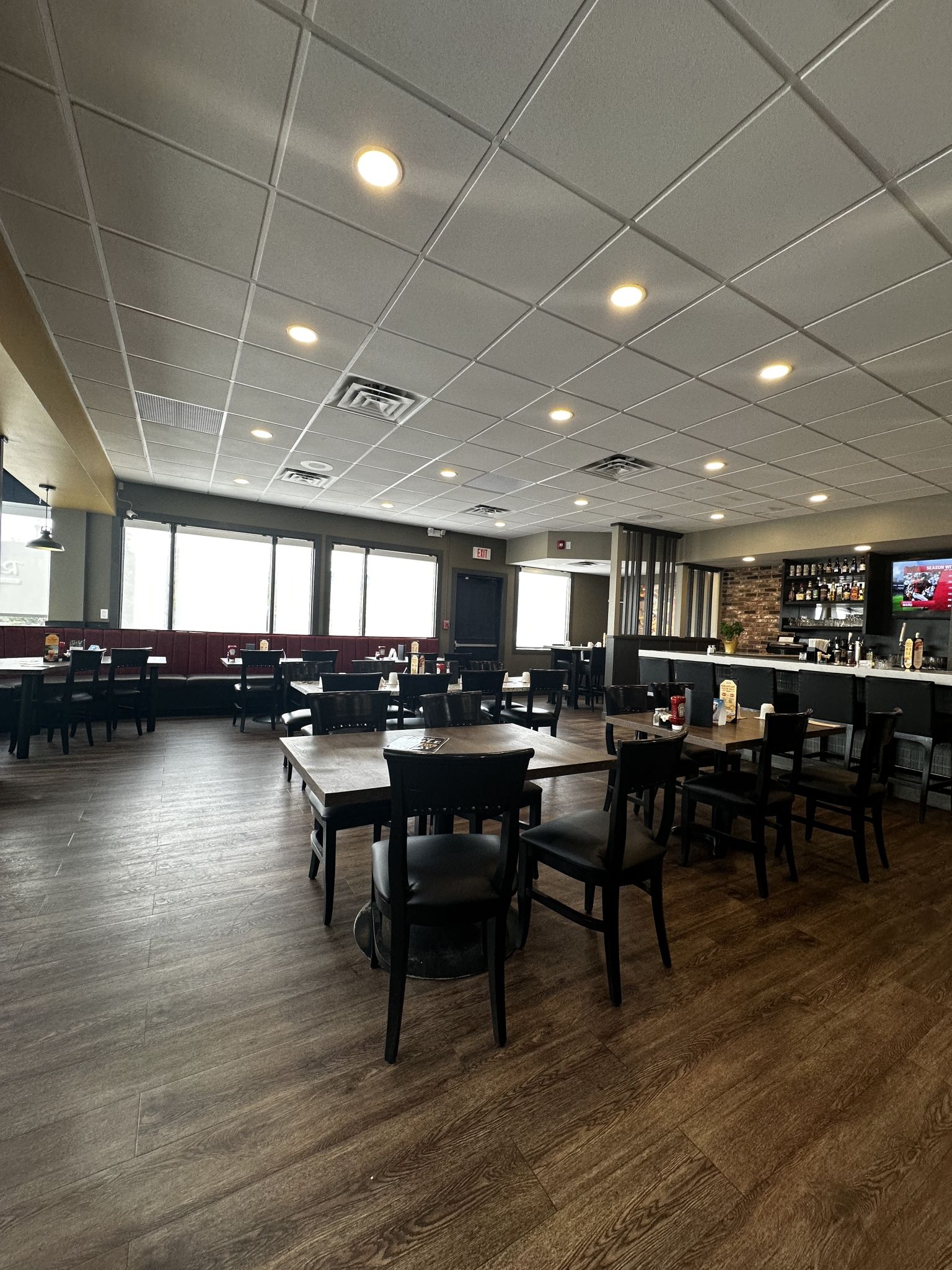 A restaurant with multiple tables and chairs, a bar area, and a television screen displaying a sports event.