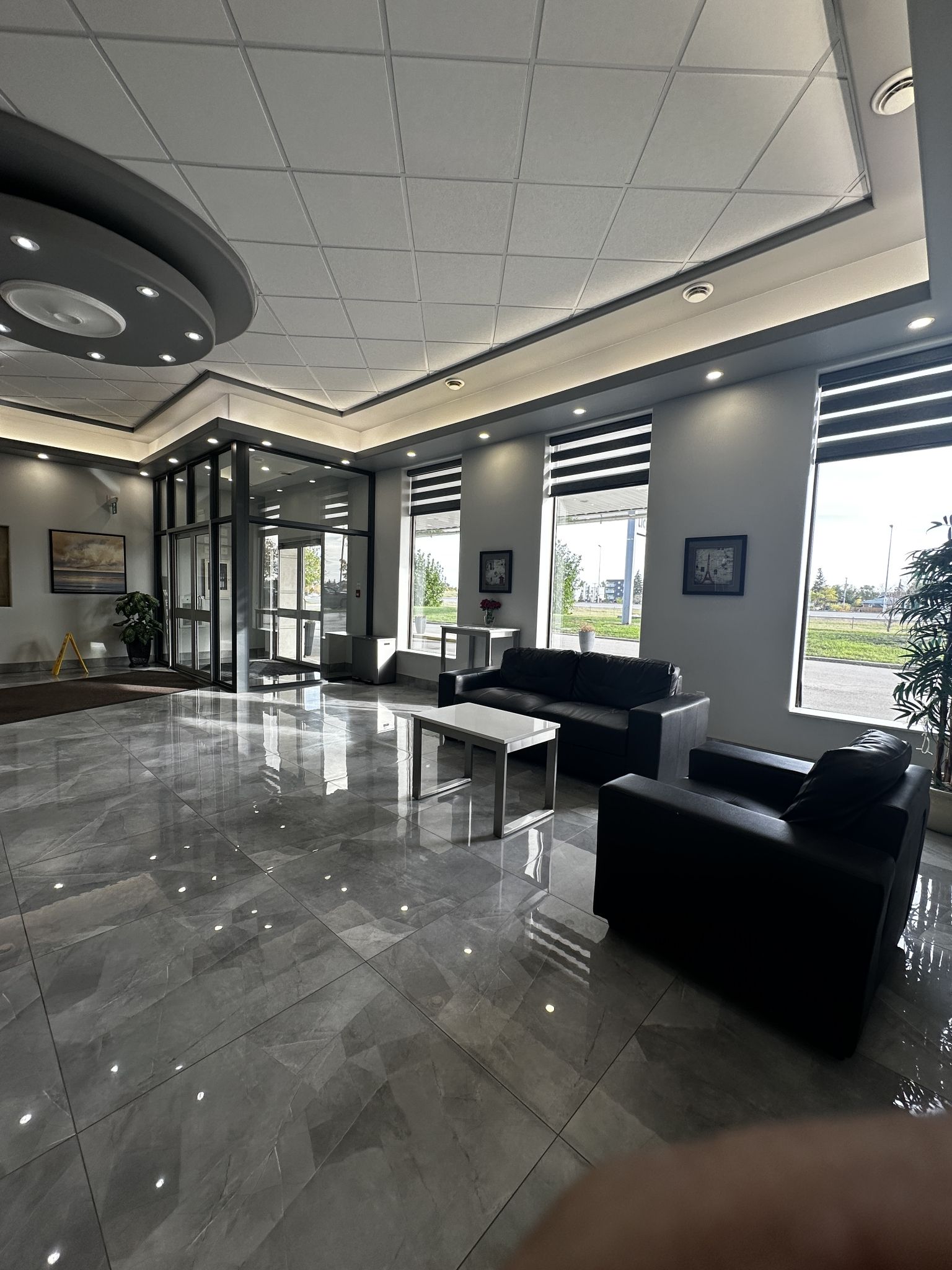 A spacious lobby with a modern design, featuring a marble floor, black leather seating, and large windows offering views of the outside.