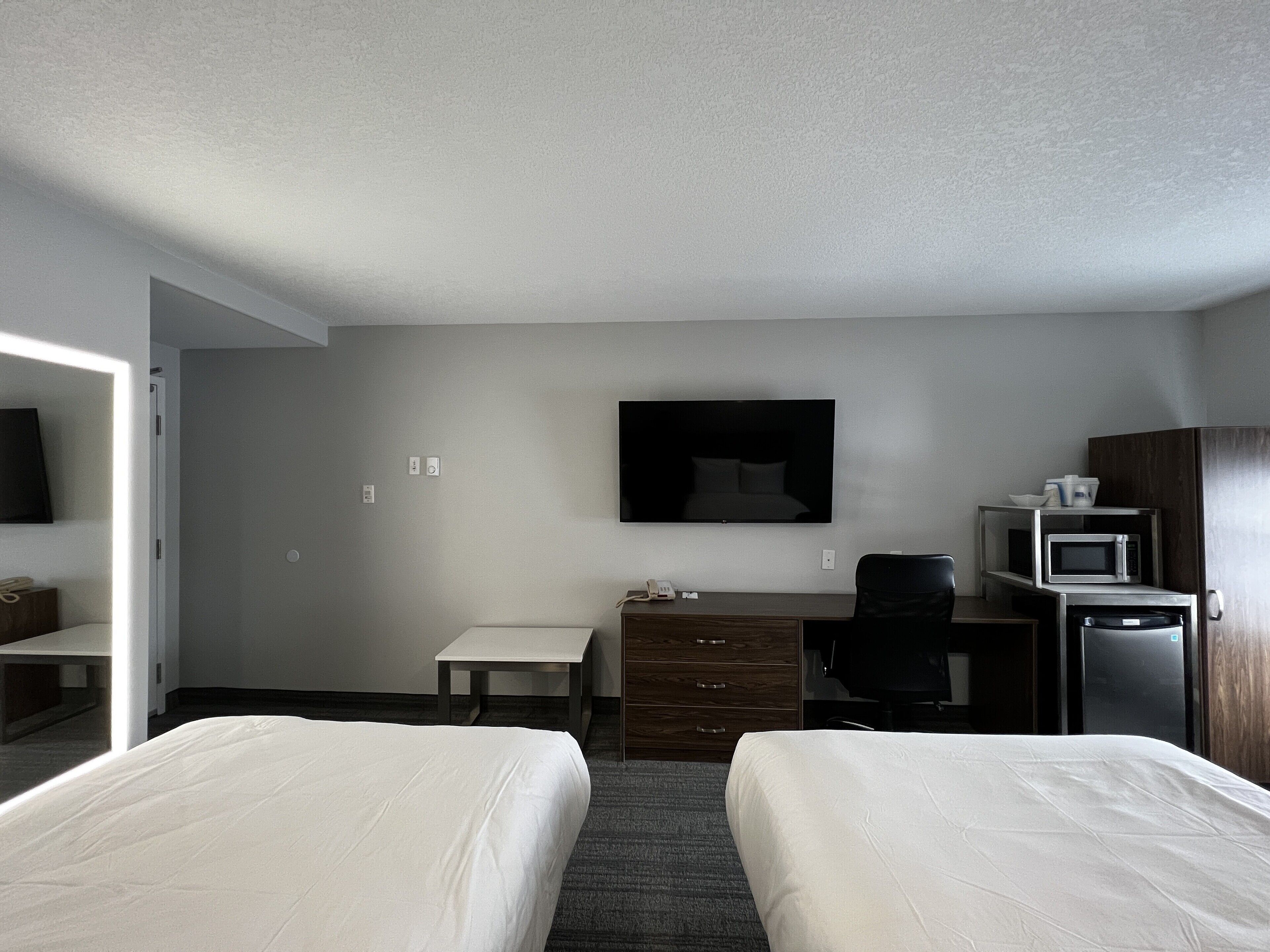 A hotel room with two beds, a desk, a chair, a flat-screen TV, a microwave, and a small refrigerator.