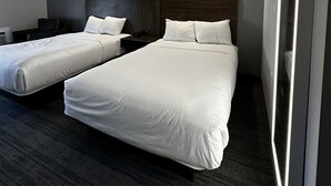 Una habitación de hotel moderna con dos camas individuales, un cabecero de madera oscura y un espejo grande.
