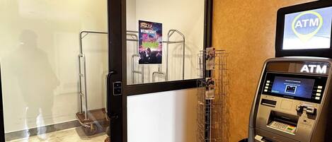 An ATM machine with a screen, a glass door entrance, and a poster advertising a karaoke event.