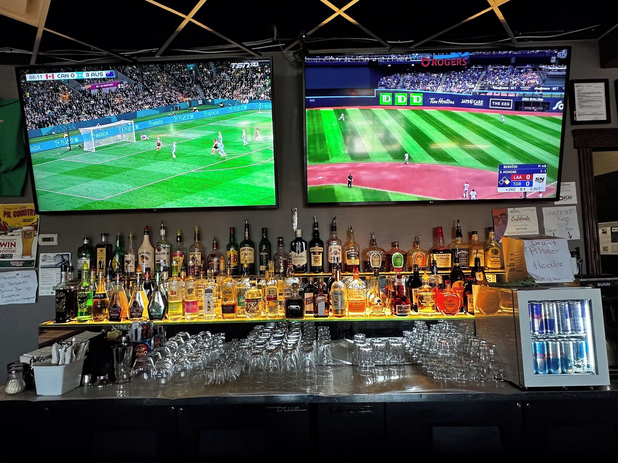 A bar area with multiple screens displaying sports events, a variety of liquor bottles, and glasses on the counter.