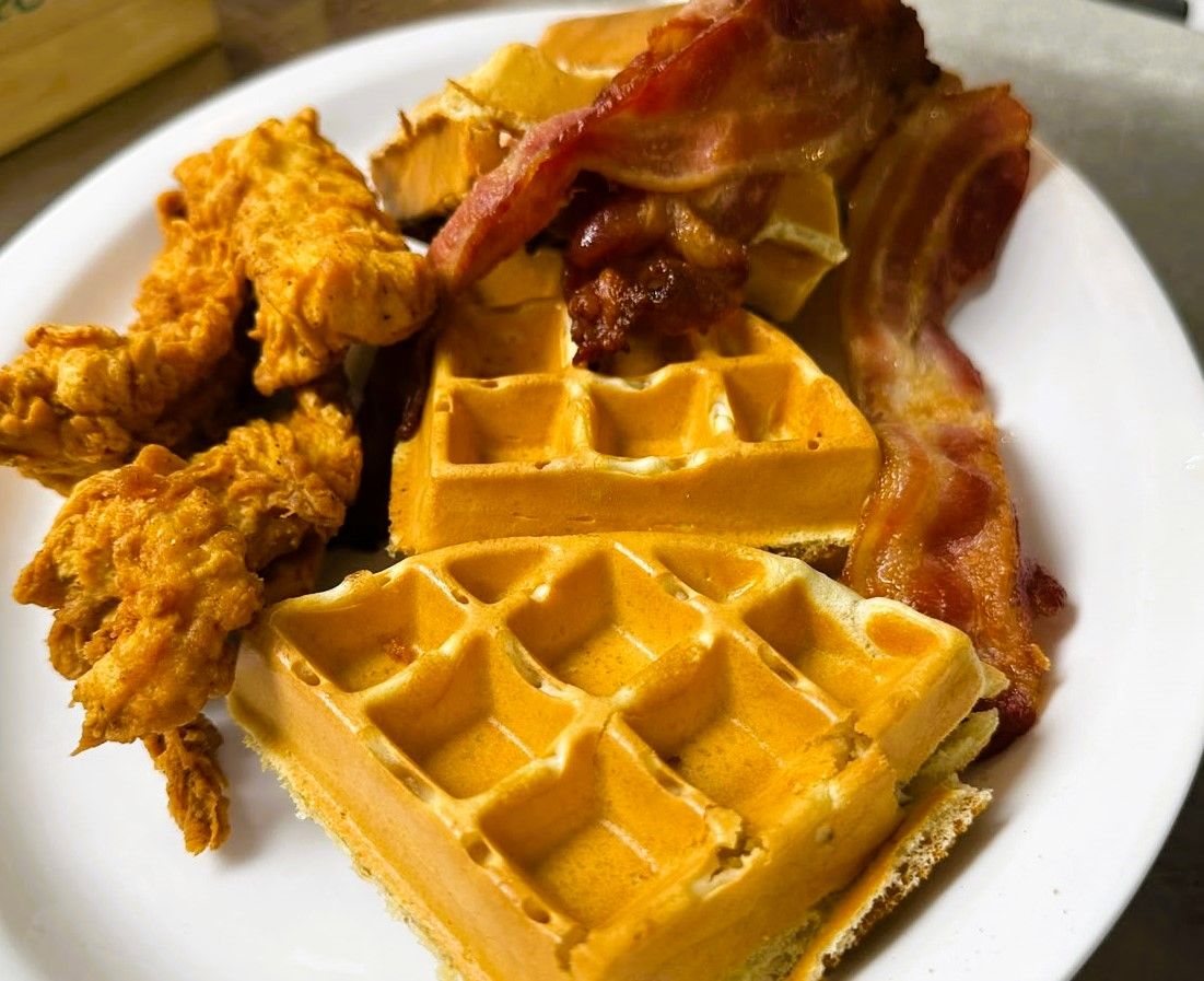 A plate with fried chicken, waffles, and bacon.