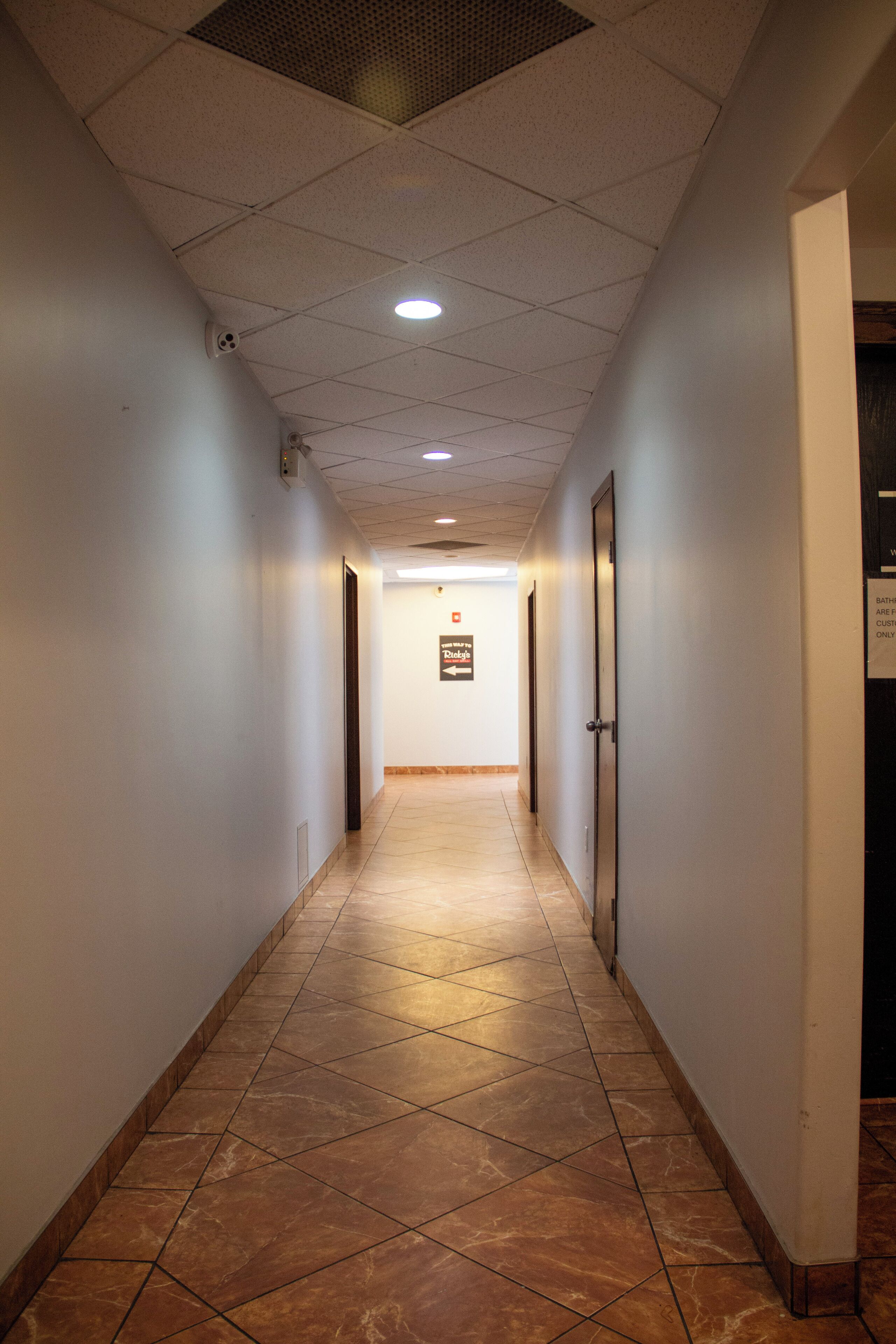 Un corridoio con pavimento piastrellato, pareti bianche e soffitto con faretti.