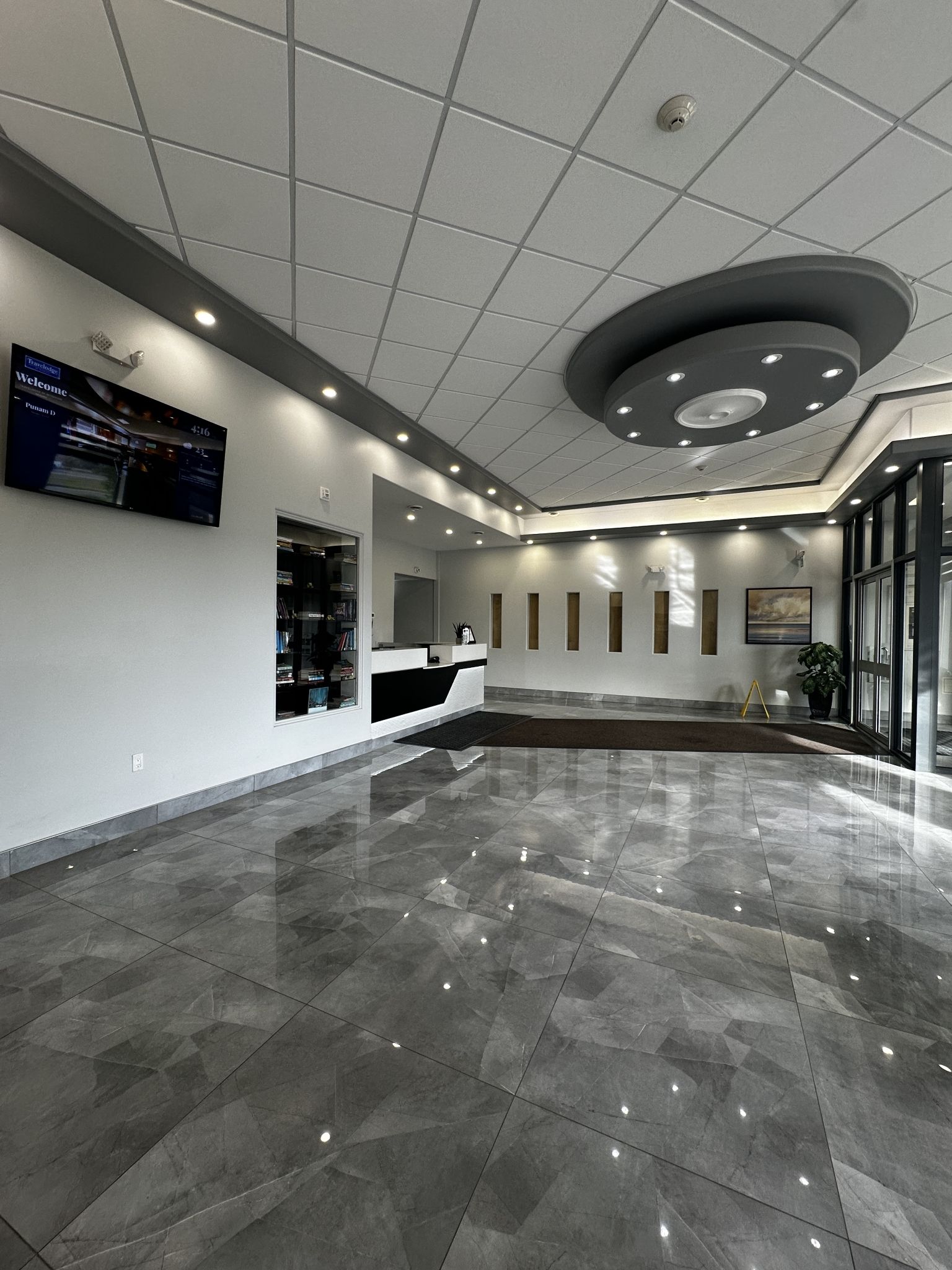 A modern lobby with a reception desk, a digital welcome screen, and a large window.