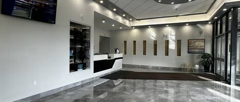 A modern lobby with a reception desk, a digital welcome screen, and a large window.