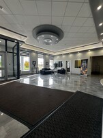Un amplio vestíbulo con diseño moderno, que presenta una zona de estar central, ventanas grandes y un piso limpio y pulido.