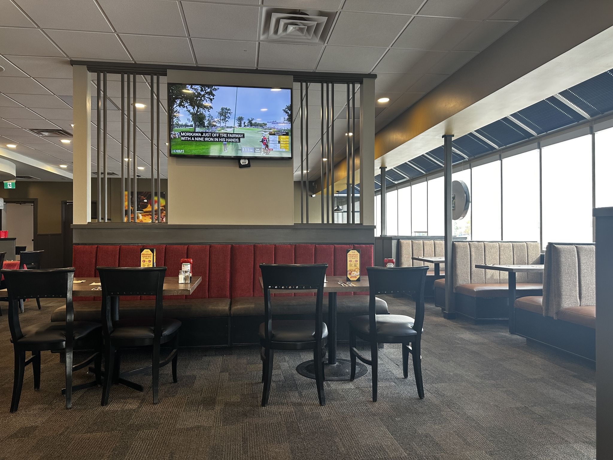 Un restaurante con cabinas y mesas, un televisor en la pared y vistas al exterior.