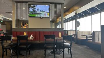 Un restaurante con cabinas y mesas, un televisor en la pared y vistas al exterior.