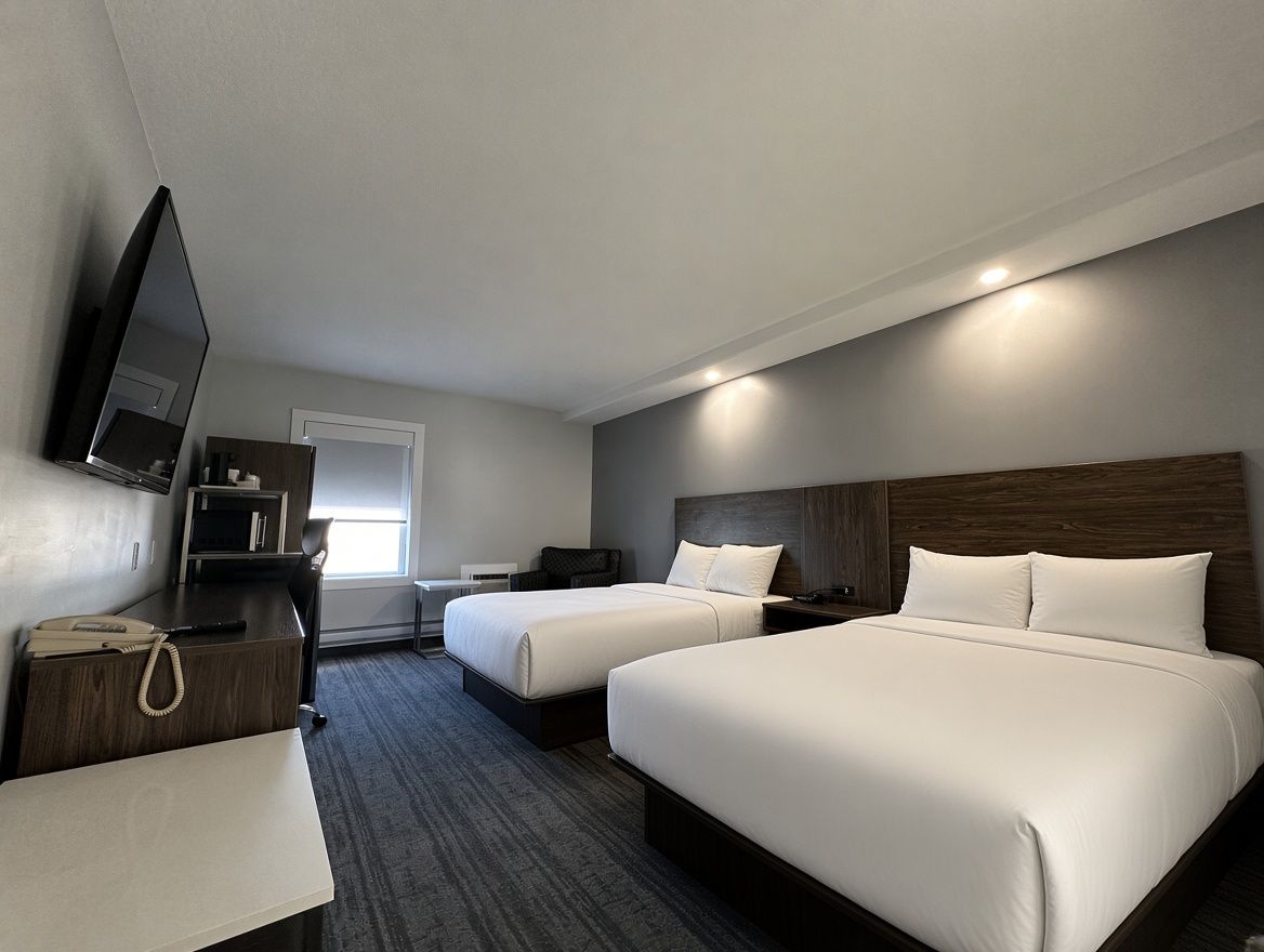 A hotel room with two beds, a desk, a chair, a television, and a window.