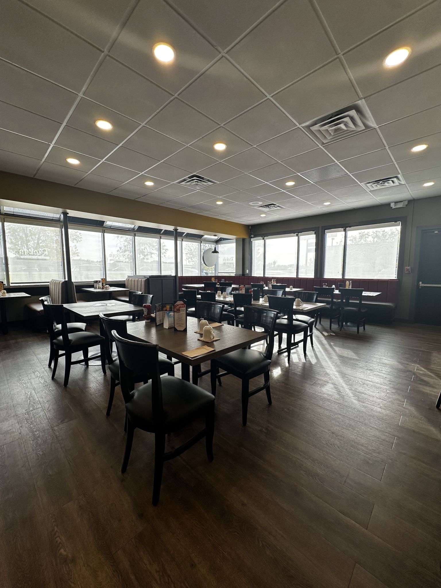 Un espace intérieur spacieux, doté de nombreuses tables et chaises, de grandes fenêtres et d’un plafond carrelé avec des luminaires encastrés.