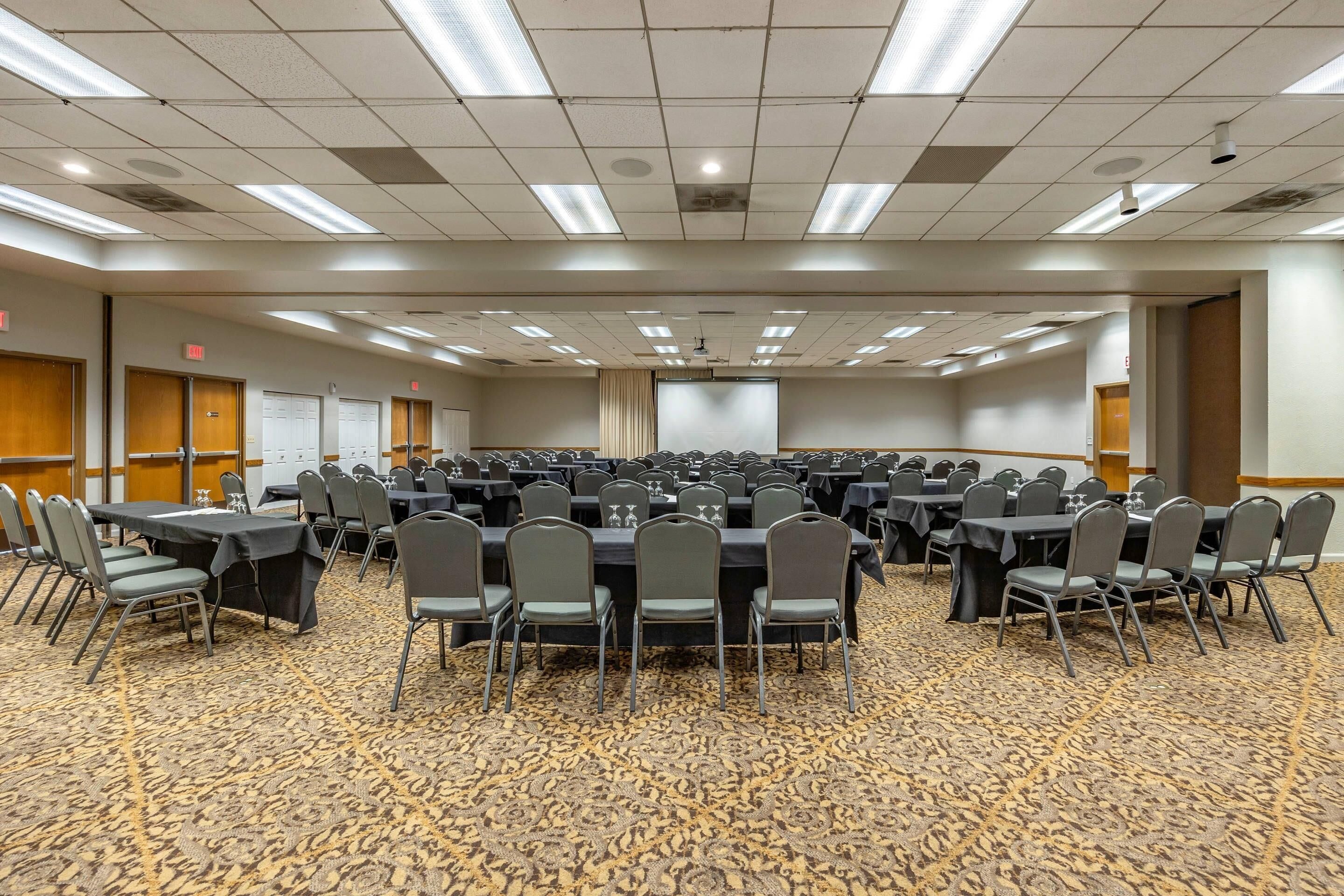A conference room with multiple tables and chairs, carpeted floor, and ceiling lights.