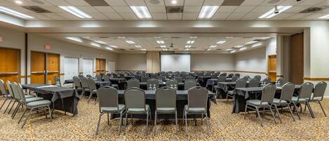 A conference room with multiple tables and chairs, carpeted floor, and ceiling lights.