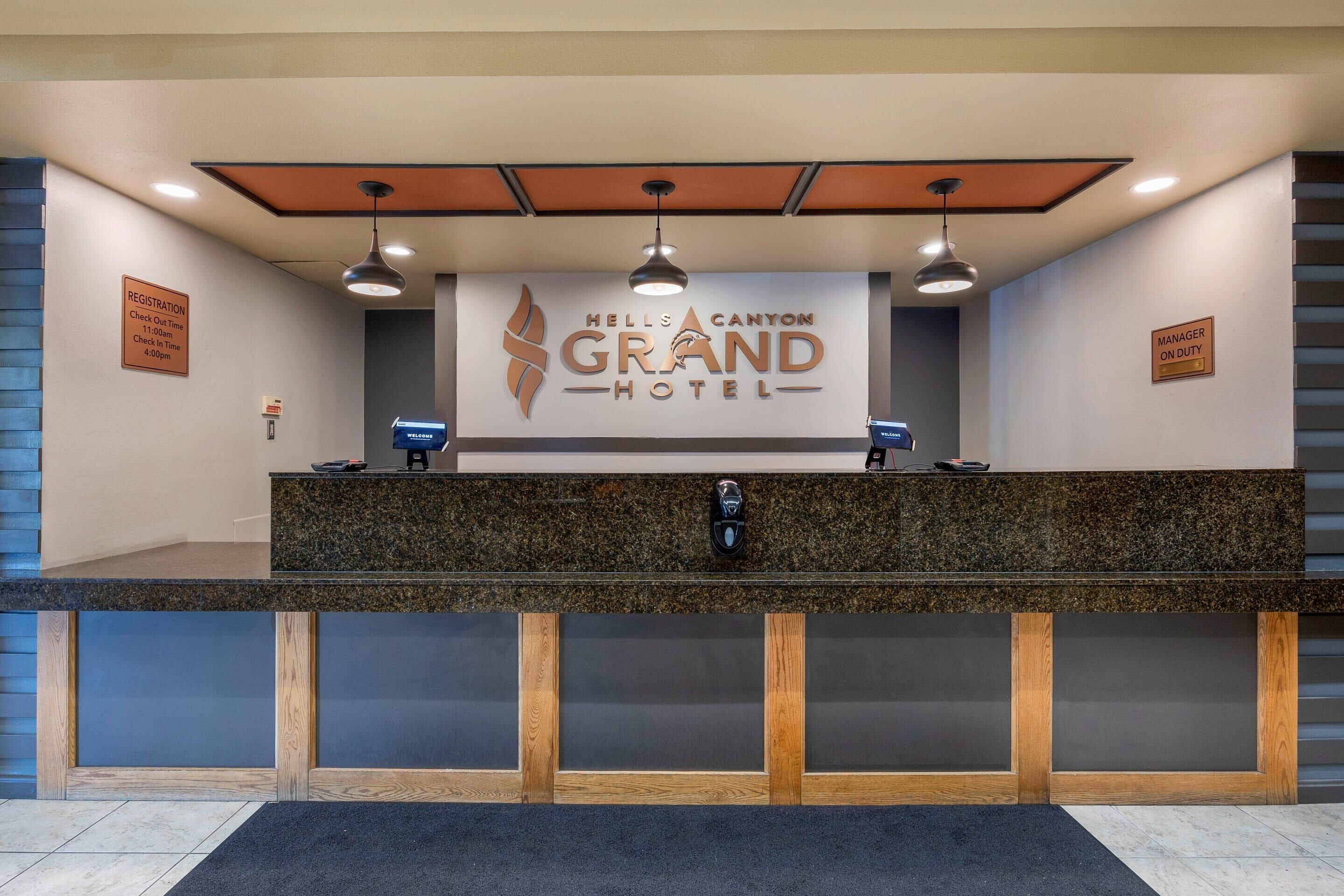 A reception desk at Hells Canyon Grand Hotel with a sign above it, a check-in counter, and a digital display.