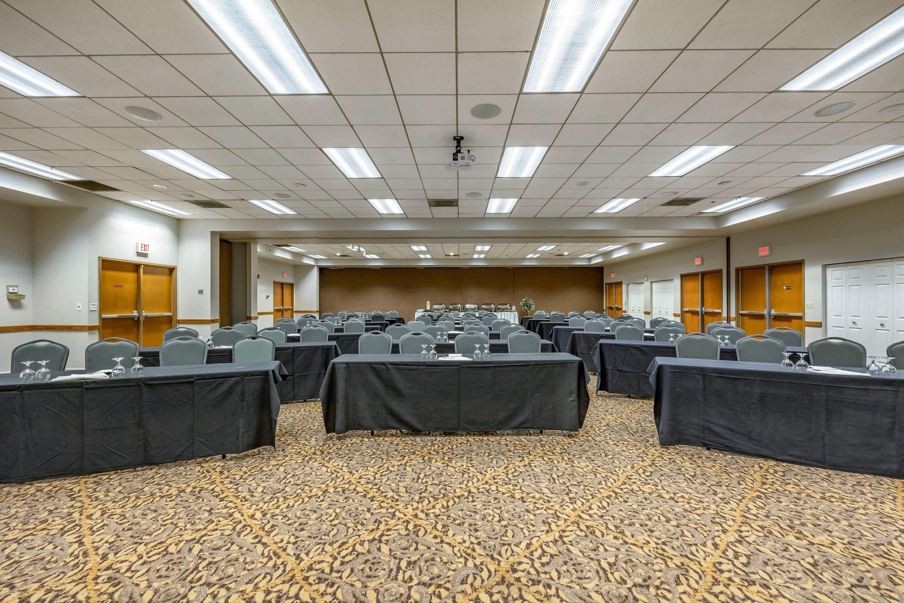A conference room with multiple tables and chairs, carpeted floor, and ceiling lights.