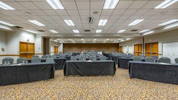 A conference room with multiple tables and chairs, carpeted floor, and ceiling lights.